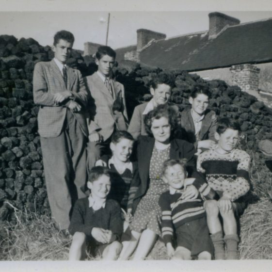The Collins Family, Clarecastle, c. 1948 A fine photo of Mrs Mai Collins and her eight sons, taken at the rear of their home in Main Street, Clarecastle. A clamp of turf as a background: Back:  Jack, Pat, Kieran, Tadg Front: Peter, Tom, Mrs Collins, Joe & Christy Photo: The Sergeant Long Collection | The Sergeant Long Collection